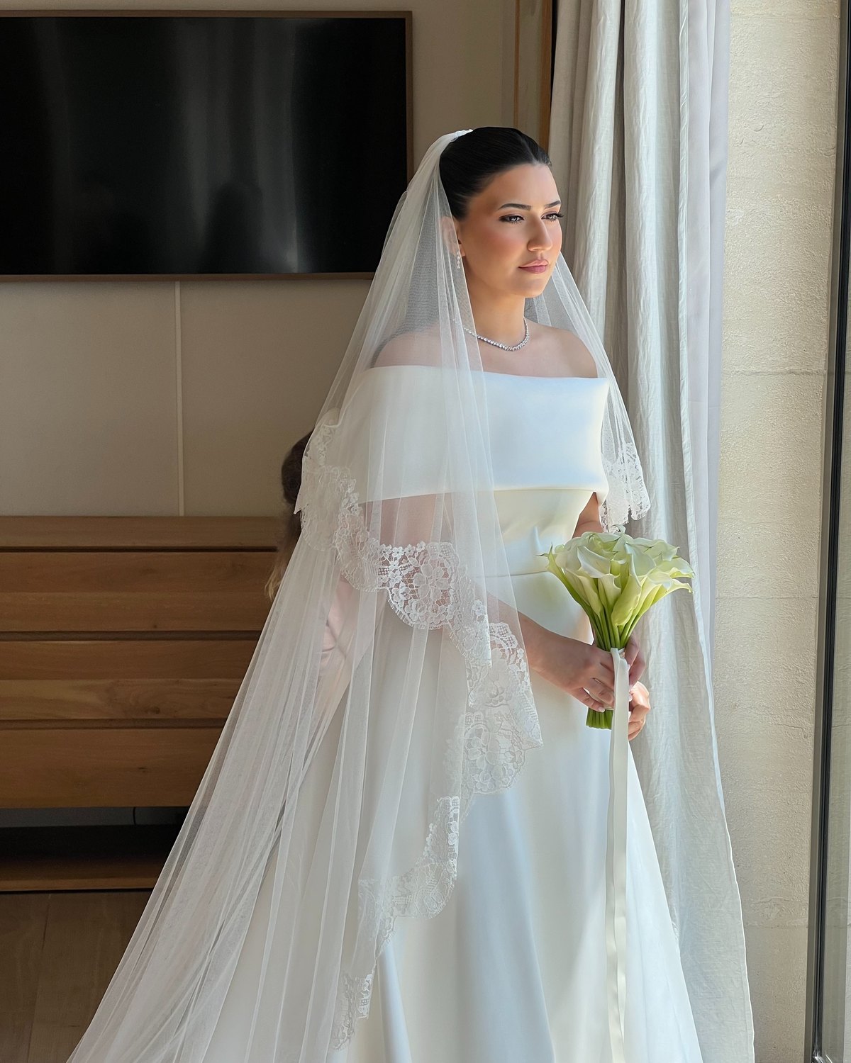 Gaindom, novia maquillada por Sanaa, bajo su velo de encaje, con un ramo de calas en la mano